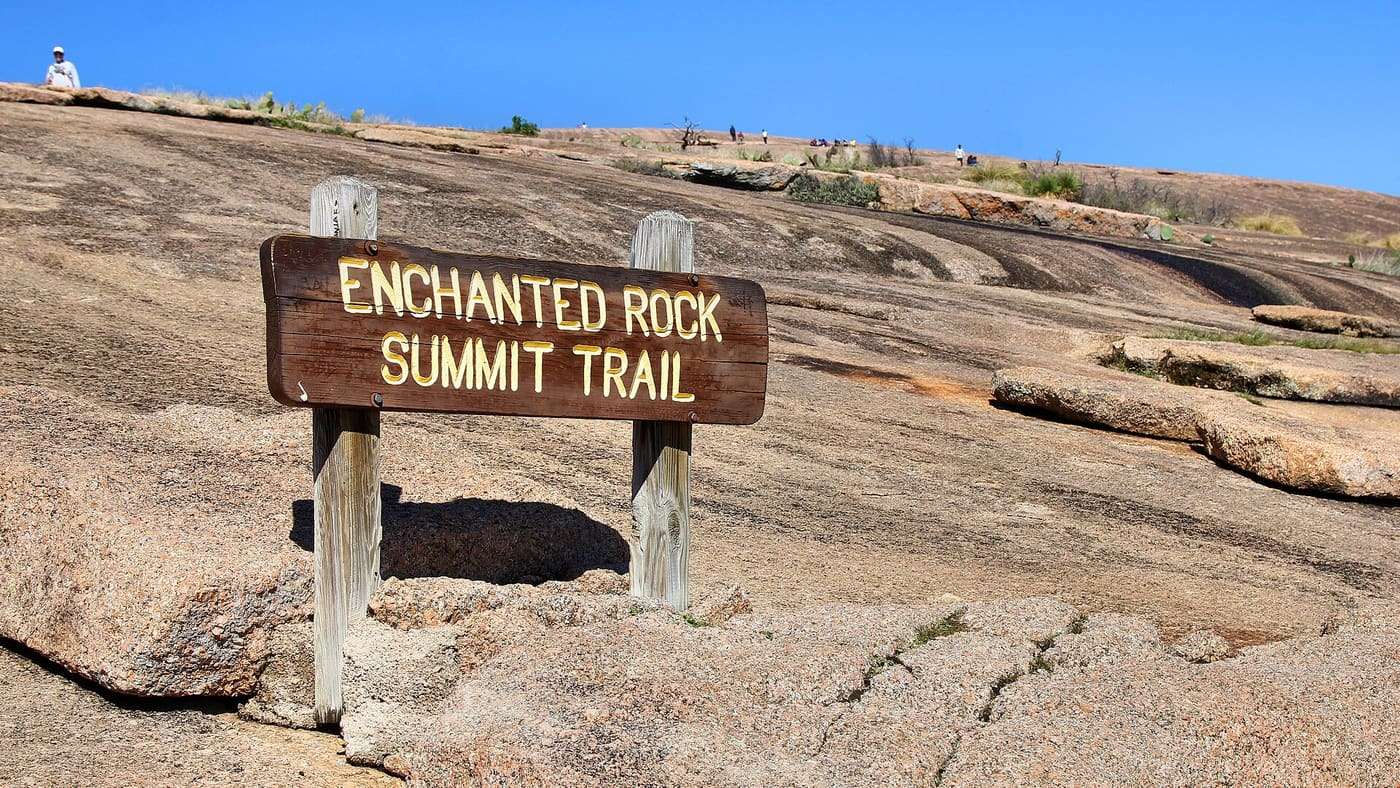Wooden Enchanted Rock Summit Trail sign set into the granite slope